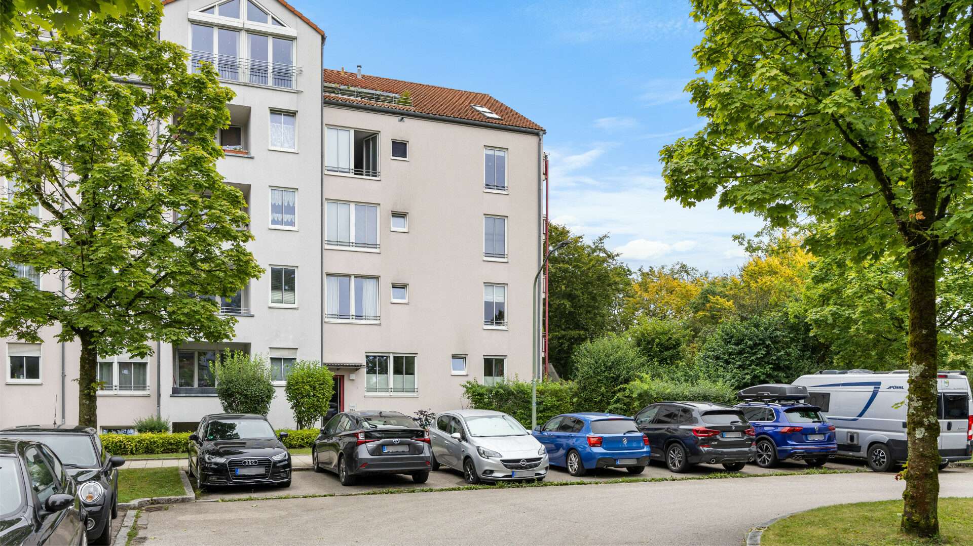 Straße mit geparkten Autos und Mehrfamilienhaus